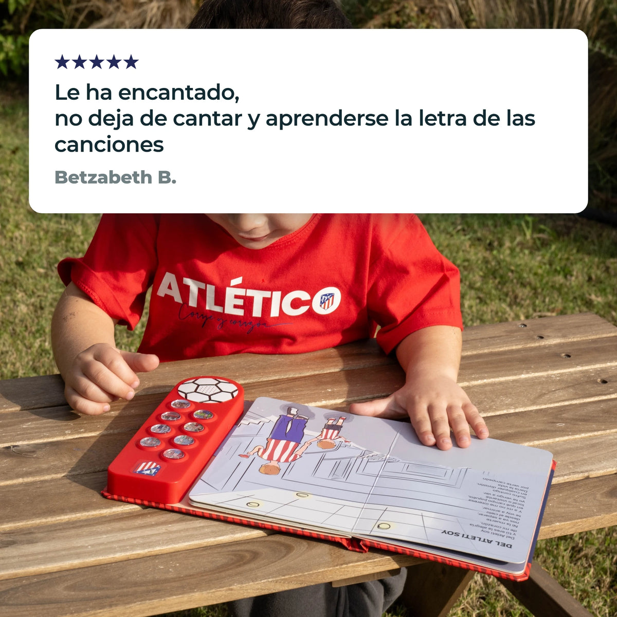 Un bambino con la maglia dell'Atlético de Madrid a un tavolo da picnic, il libro sonoro aperto davanti e entrambe le mani sopra, accanto a una recensione a cinque stelle di un cliente.