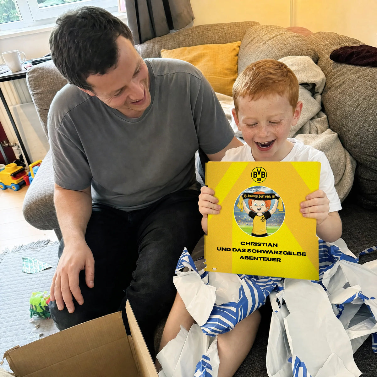 Un padre e suo figlio sul divano, il Libro Personalizzato del Borussia Dortmund appena uscito dalla carta da regalo.