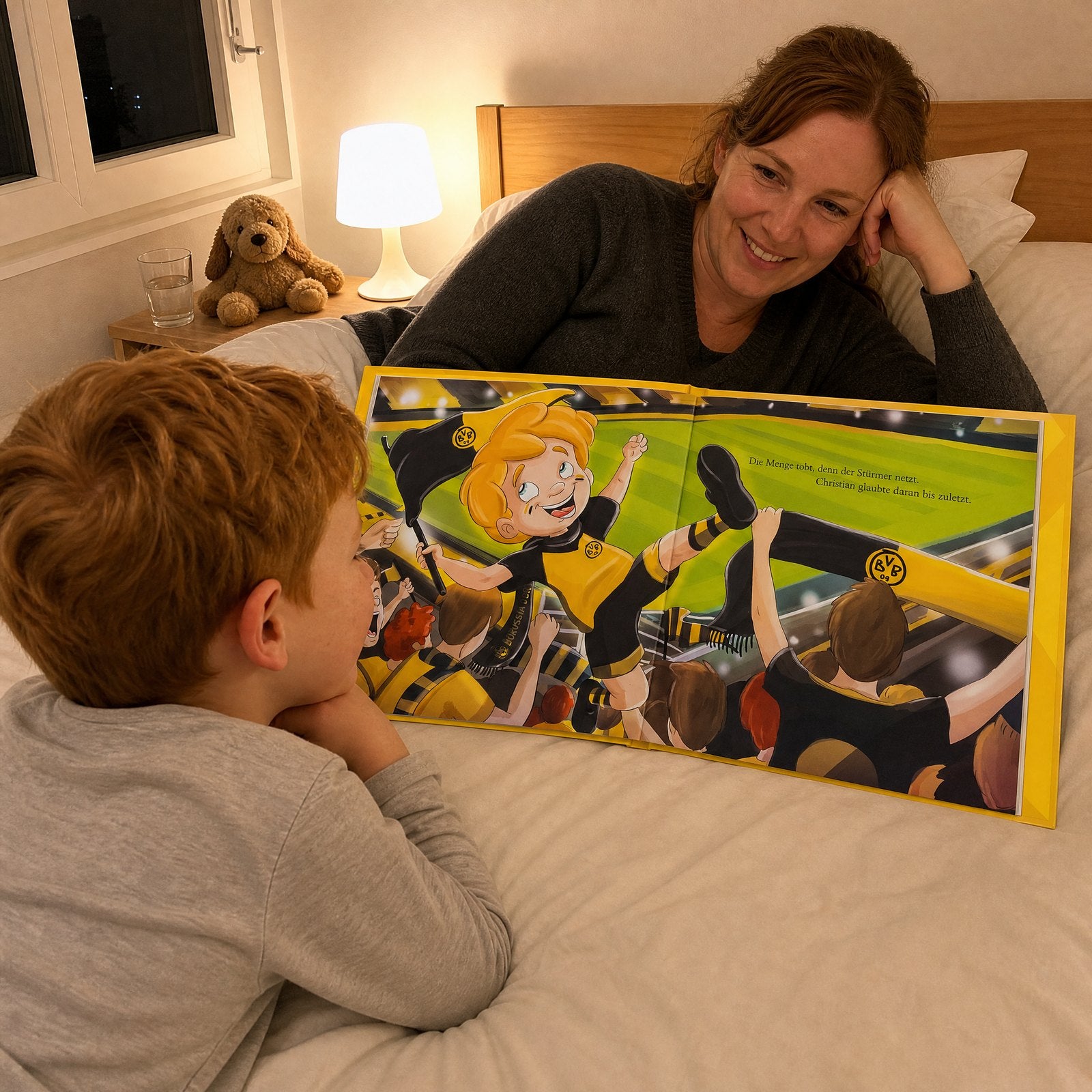 A young boy lying on his bed at night reading the Borussia Dortmund Personalised Book while his mum watches him and smiles.