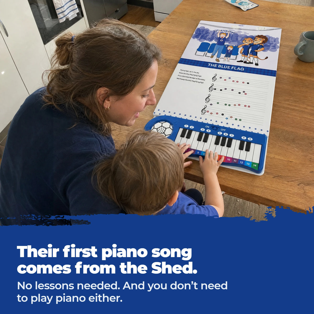 Un bambino in braccio alla mamma, al tavolo, suona i tasti del Libro di Pianoforte del Chelsea, aperto e steso davanti a loro.