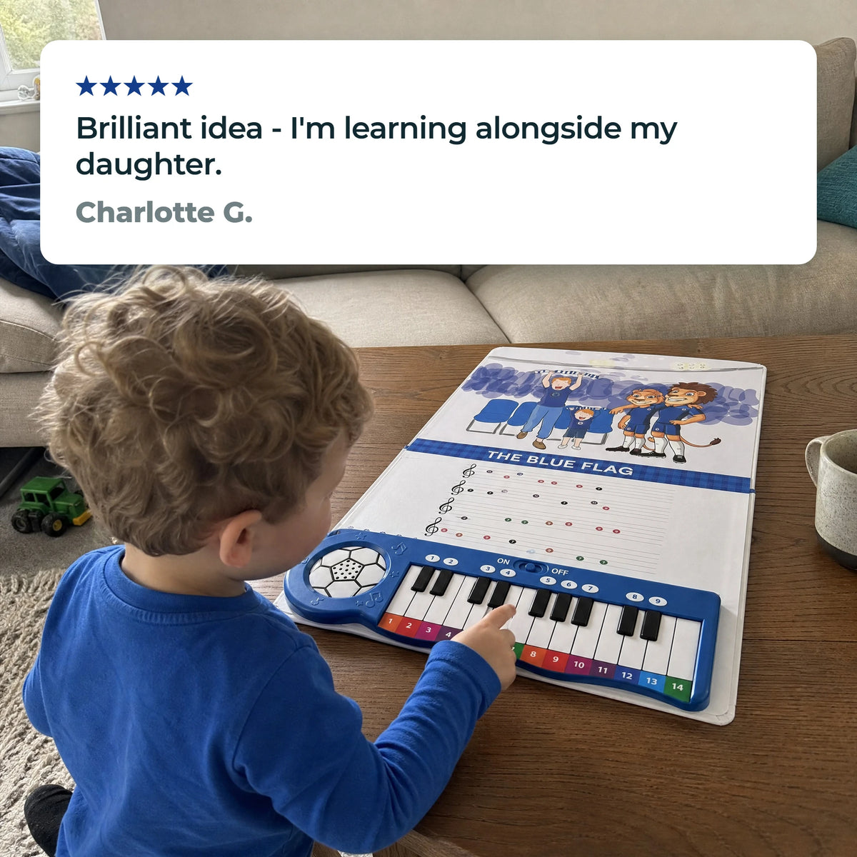 Un bambino piccolo suona i tasti del Libro di Pianoforte del Chelsea, aperto e steso su un tavolino, sotto una recensione a cinque stelle di Charlotte G.: «Brilliant idea - I'm learning alongside my daughter.»
