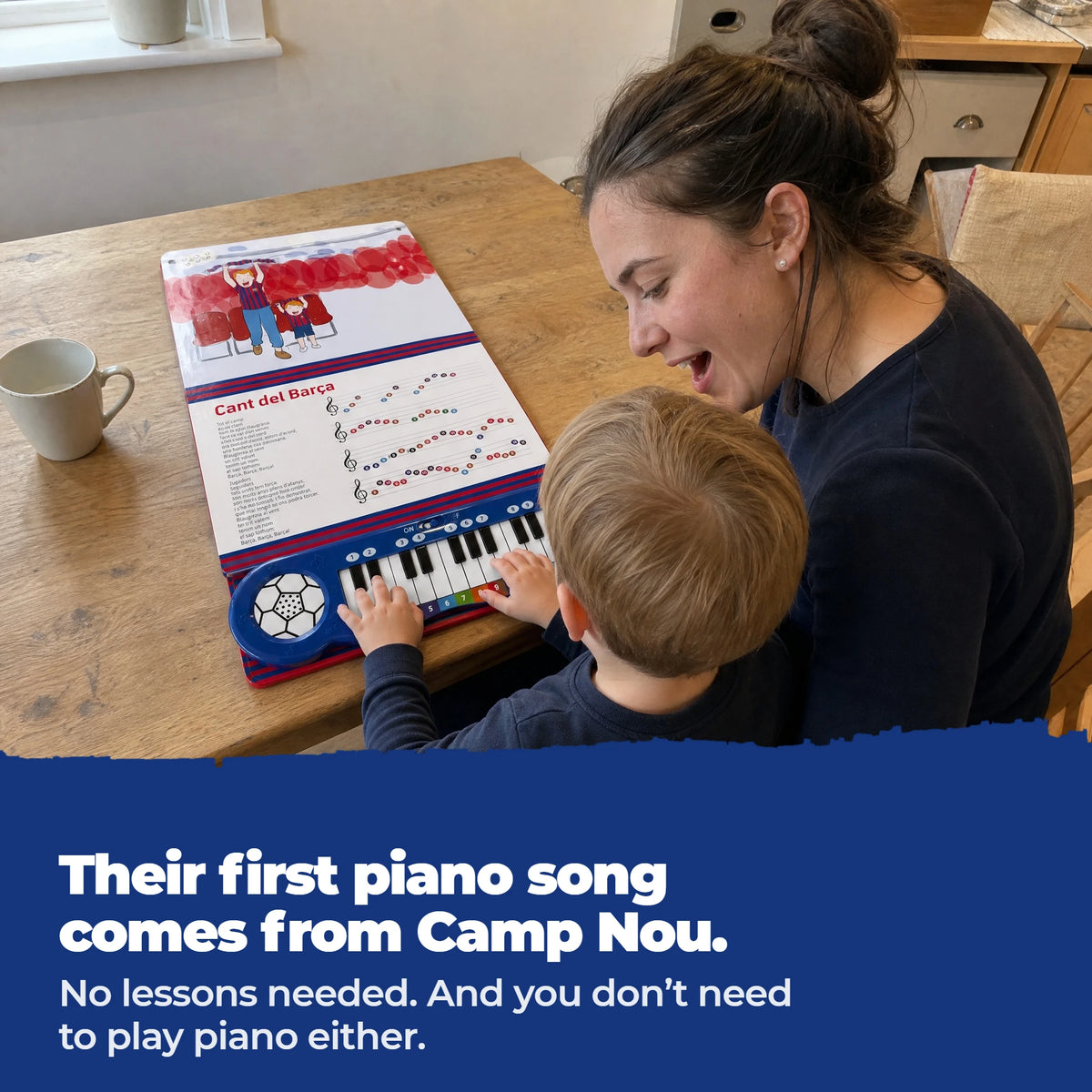 Un bambino in braccio alla mamma, al tavolo, suona i tasti del Libro di Pianoforte del Barça, aperto e steso davanti a loro.
