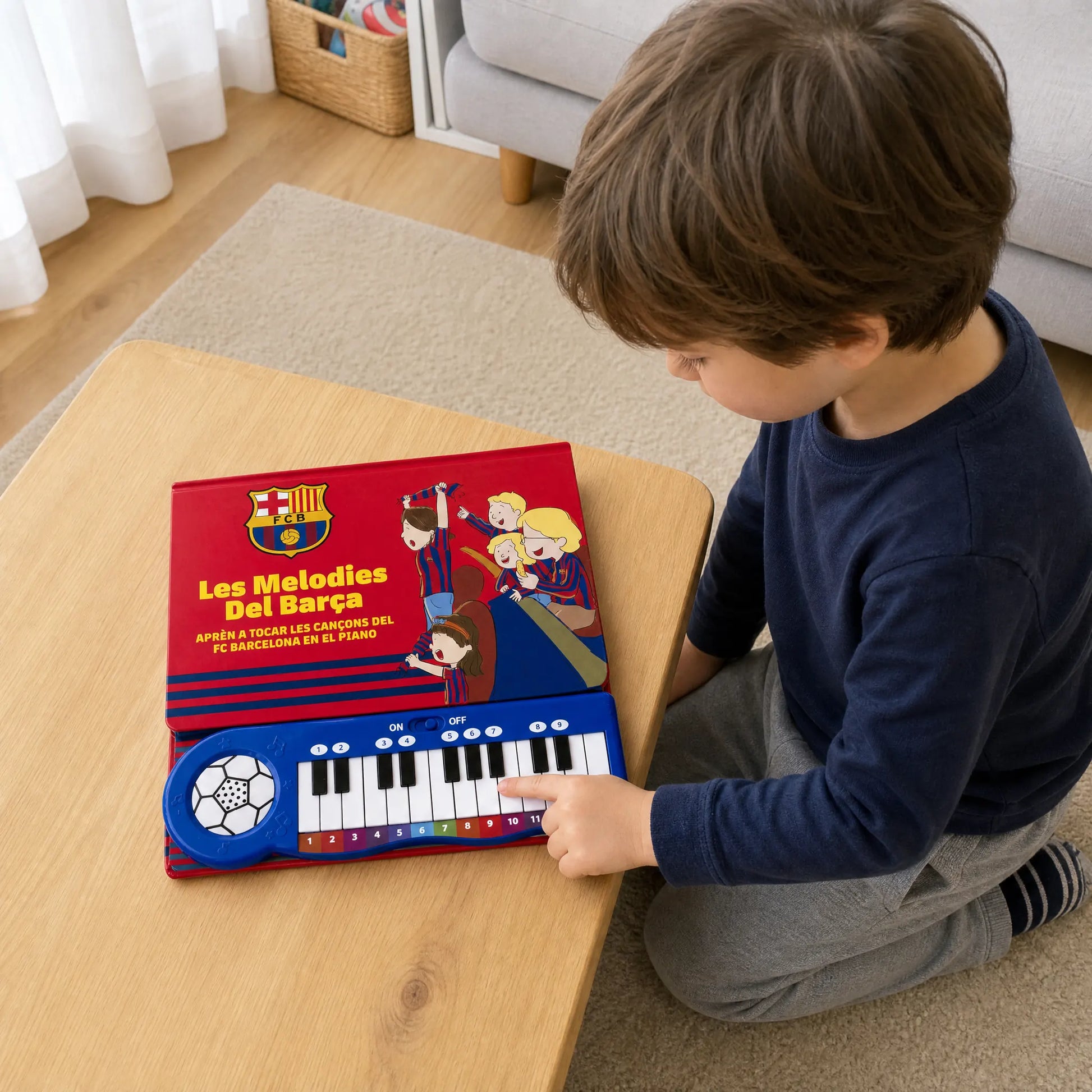 A child kneeling at a low table, playing the keys of the FC Barcelona Piano Book as it lies flat in front of them.
