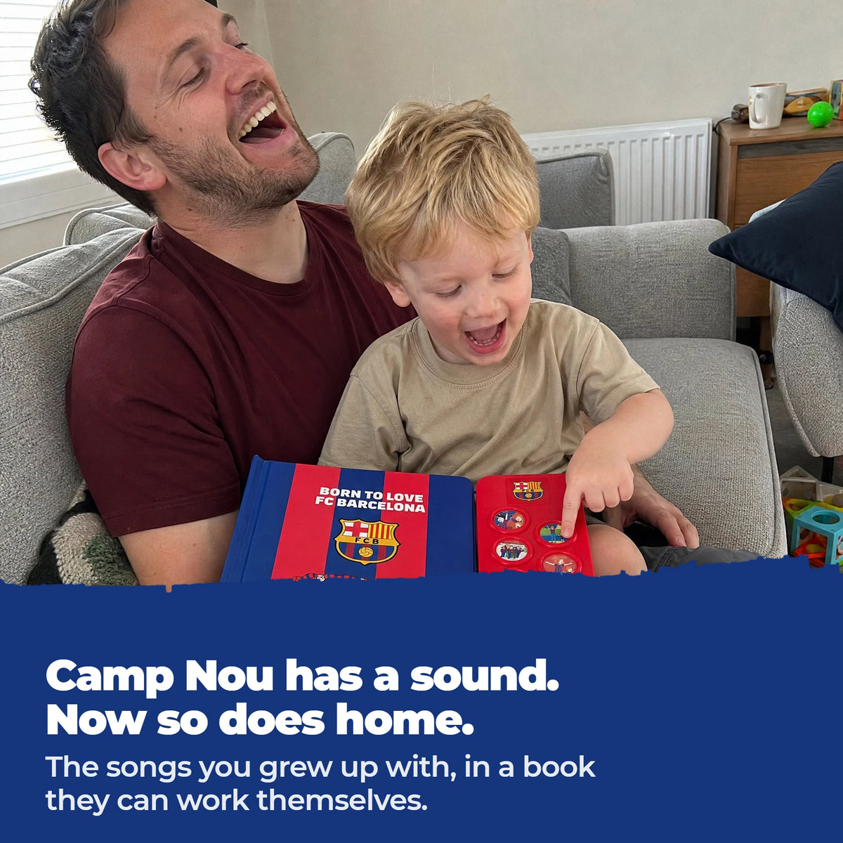 Un padre y su hijo pequeño en el sofá cantan juntos sobre el libro musical del FC Barcelona abierto, con el dedo del niño en uno de los botones de sonido.