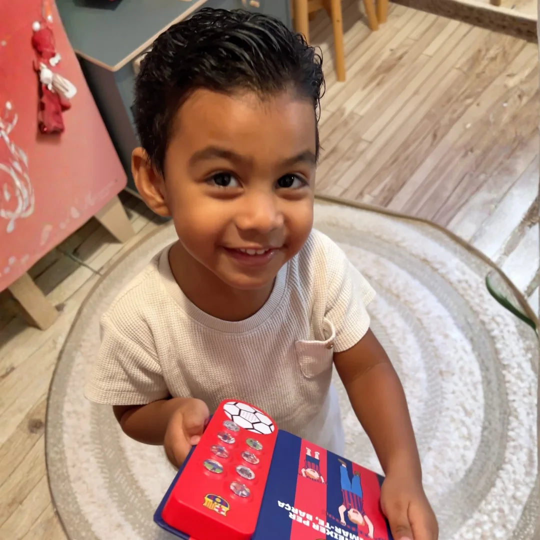 A child sitting on the rug holding the FC Barcelona Sound Book.