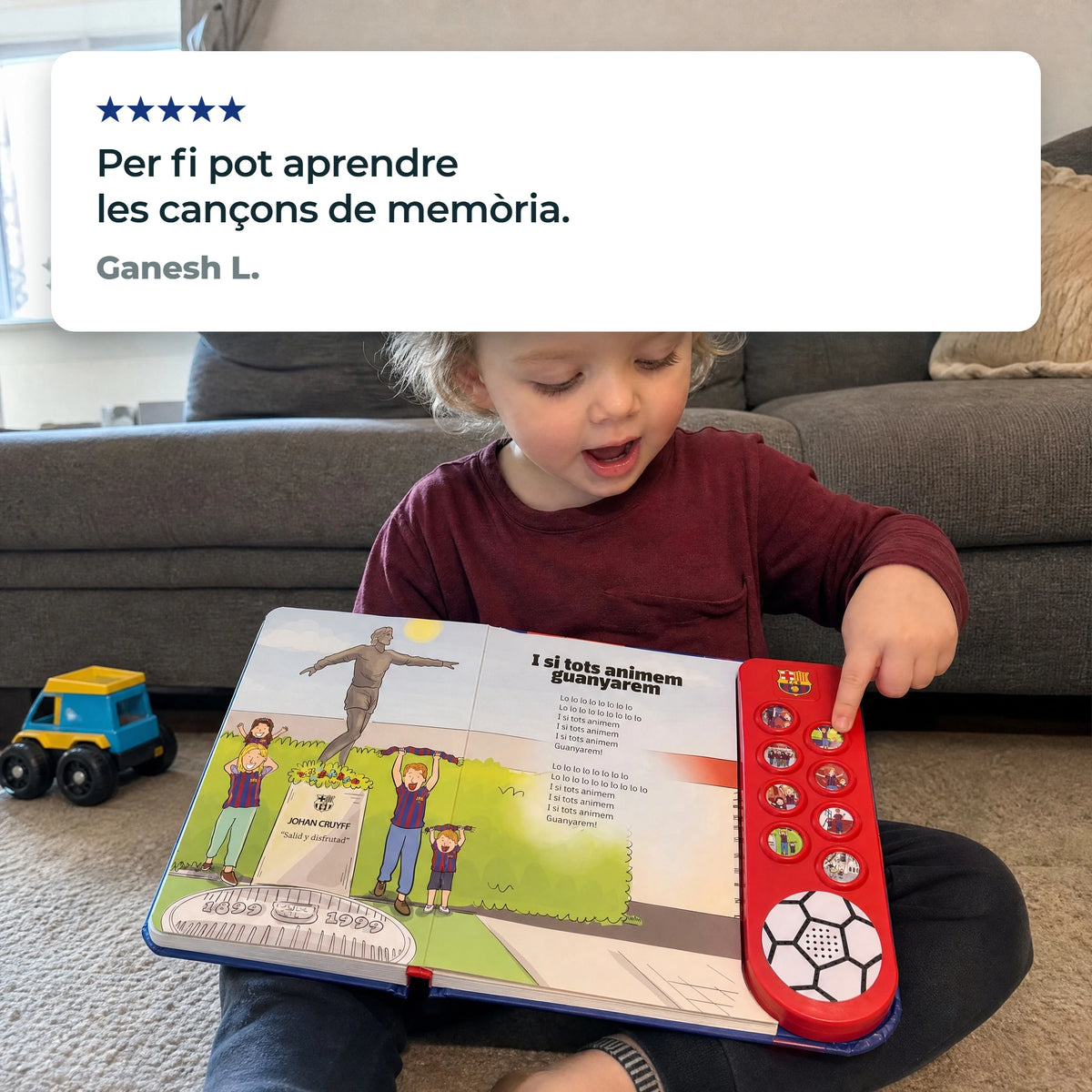 Un bambino con l'edizione in catalano del libro sonoro dell'FC Barcelona aperta su I si tots animem guanyarem sulle ginocchia, un dito su un pulsante, accanto a una recensione a cinque stelle di un cliente in catalano.