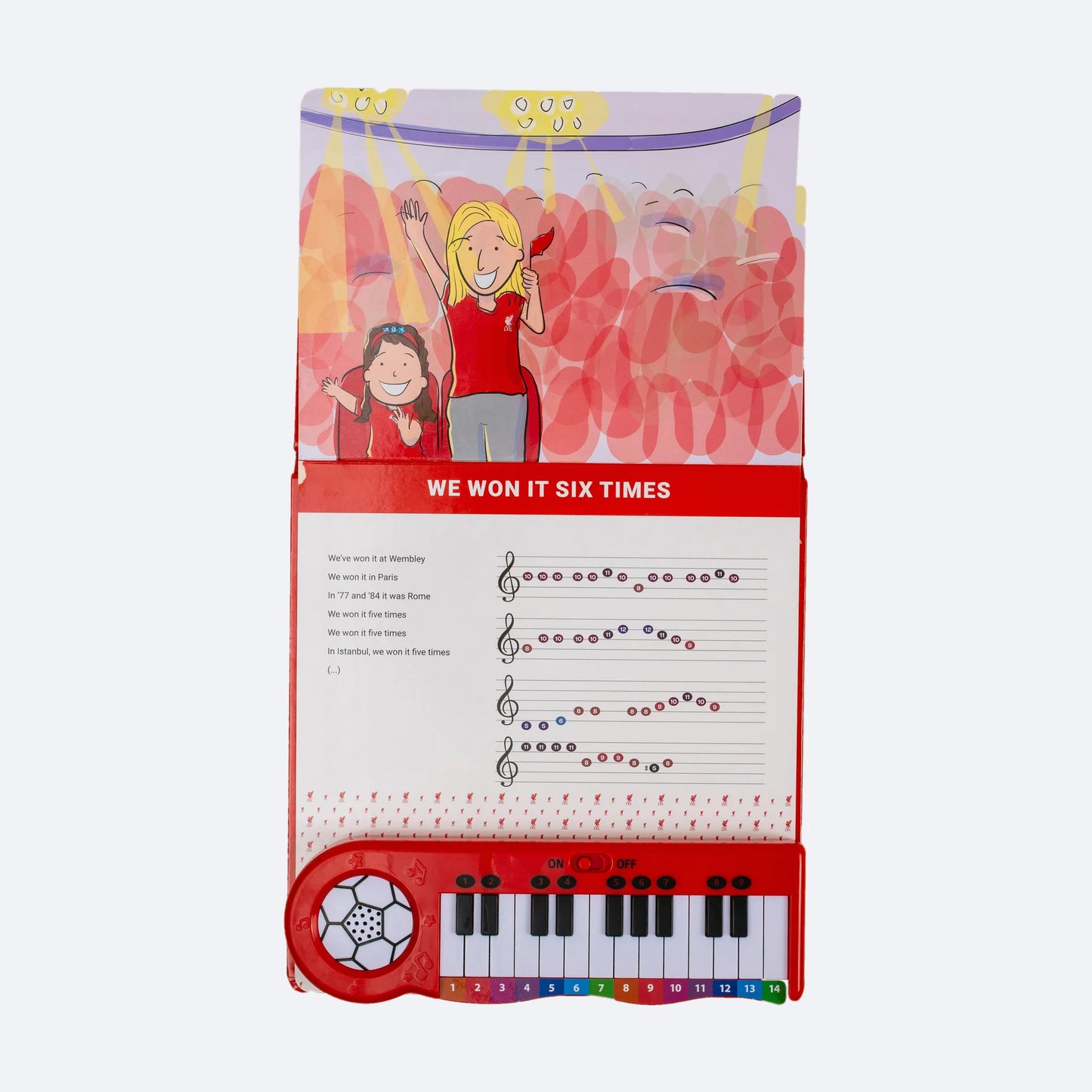 The Liverpool FC Piano Book open, showing an illustrated spread with colour-coded sheet music above the keyboard.