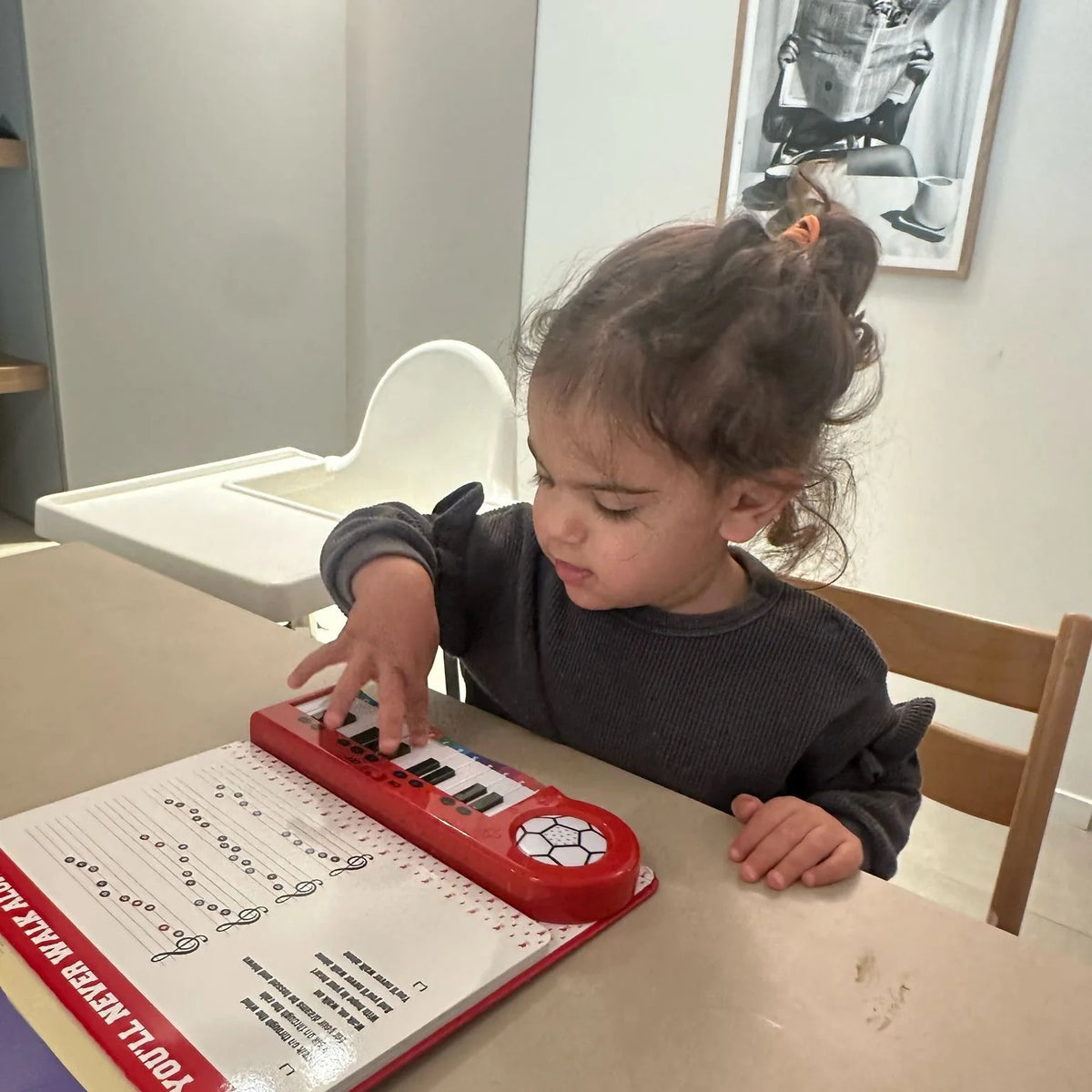 A toddler playing the Liverpool FC Piano Book at the kitchen table.