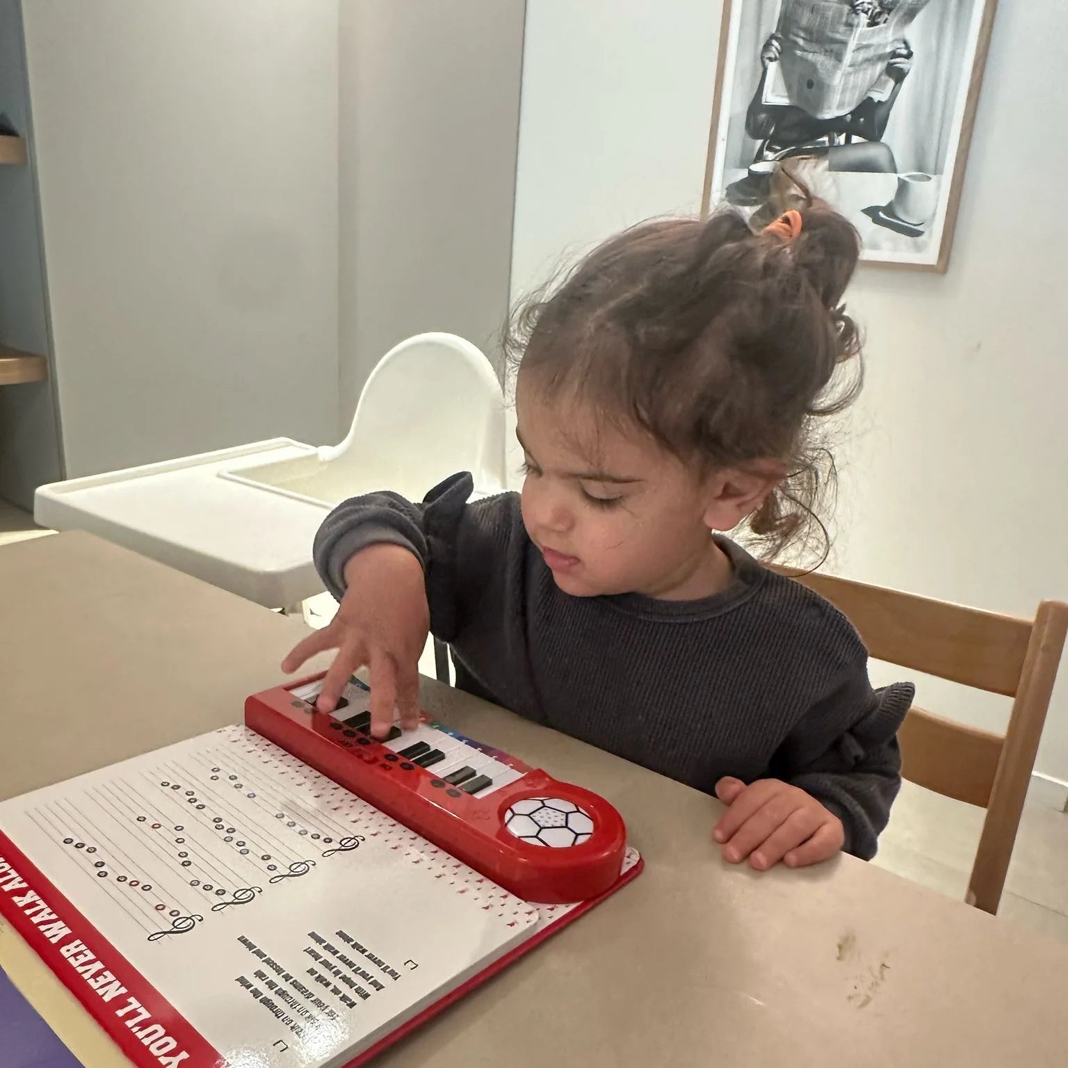 A toddler at a table with one hand on the keys of the Liverpool Piano Book, concentrating.