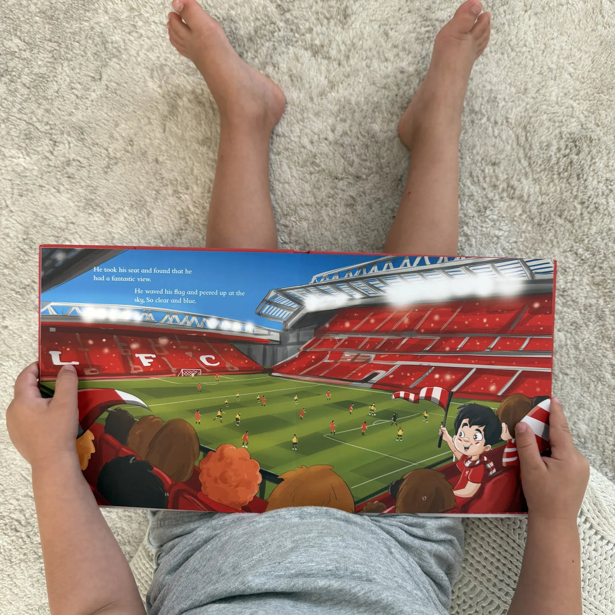 A child sitting on the floor at home reading the Liverpool FC Personalised Book, open at the Anfield spread.