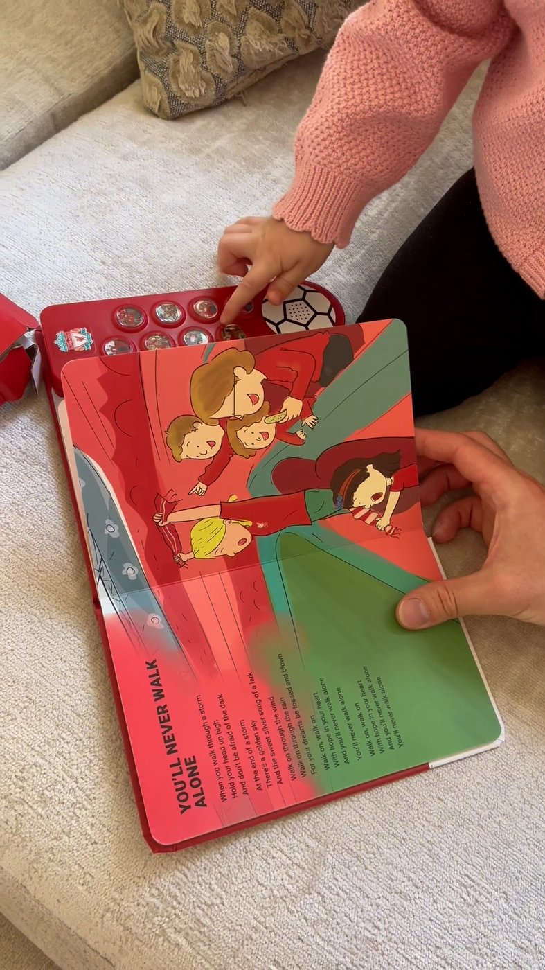 A toddler presses a button on the Liverpool FC Sound Book, open at You'll Never Walk Alone