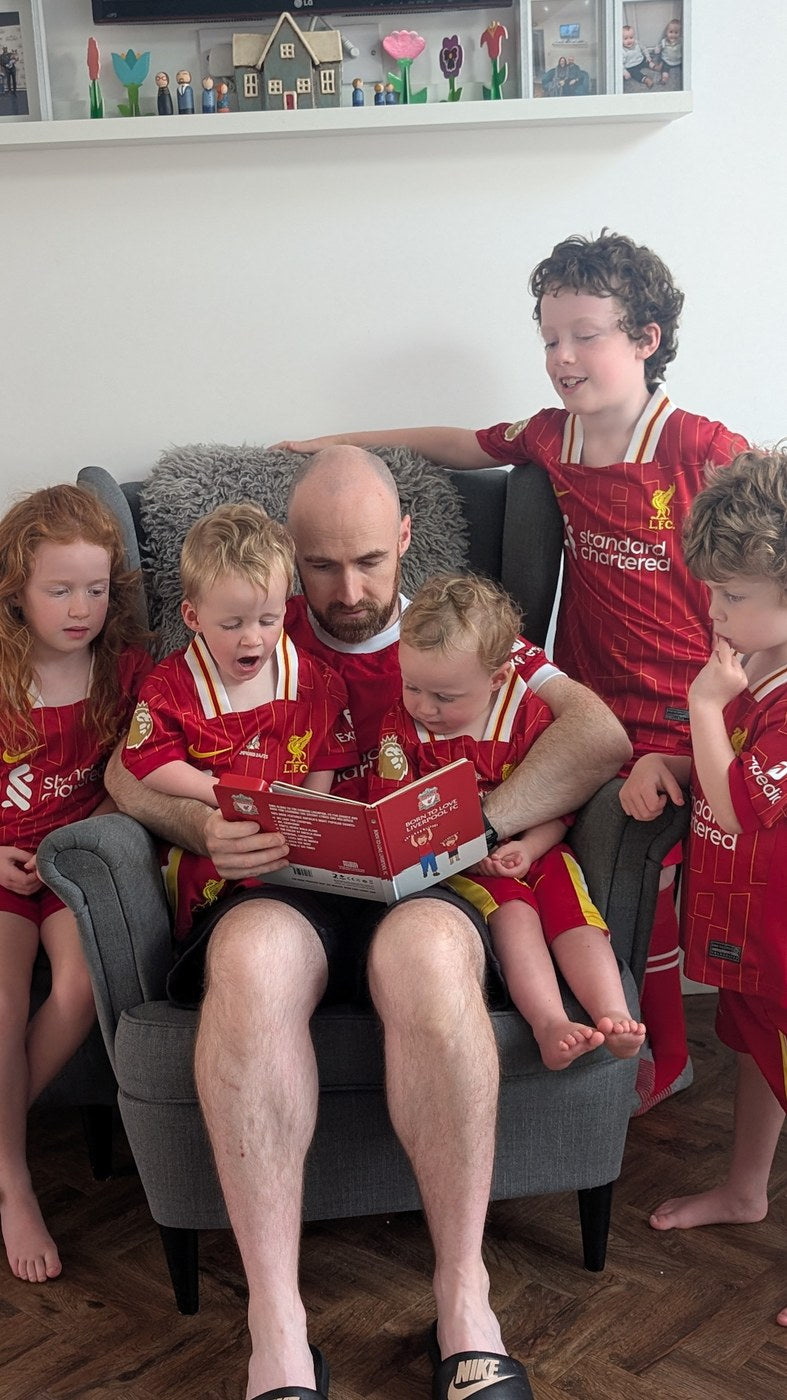 A Liverpool supporter reads the Sound Book in an armchair with five children, all in LFC kit