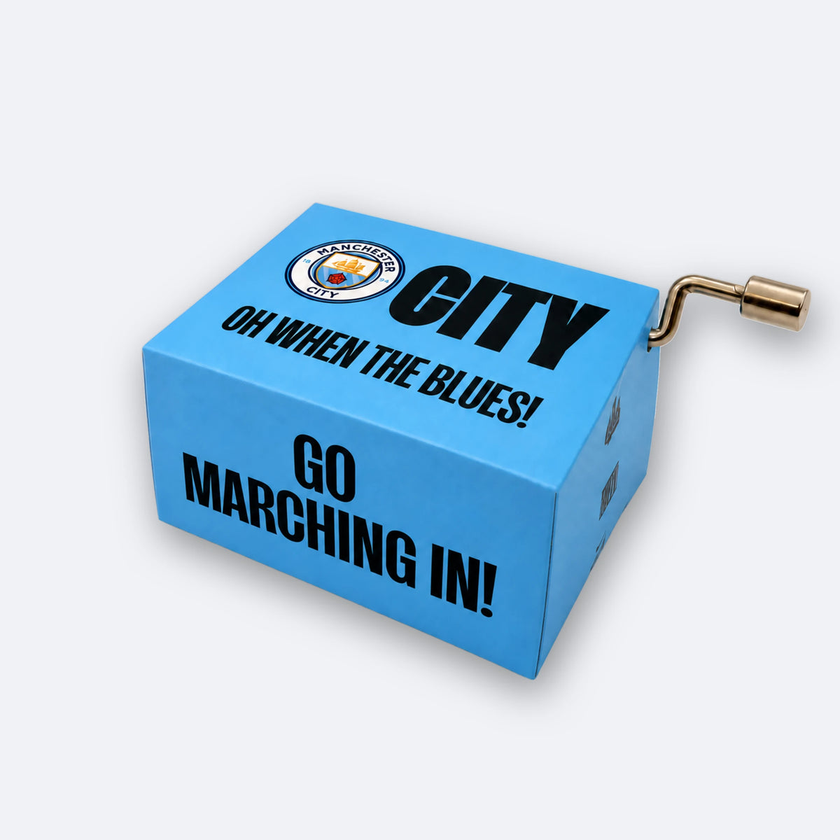 Caja de música con manivela del Manchester City: una caja azul celeste con el escudo del club y CITY, OH WHEN THE BLUES! y GO MARCHING IN! impresos, con una pequeña manivela metálica en el lateral.