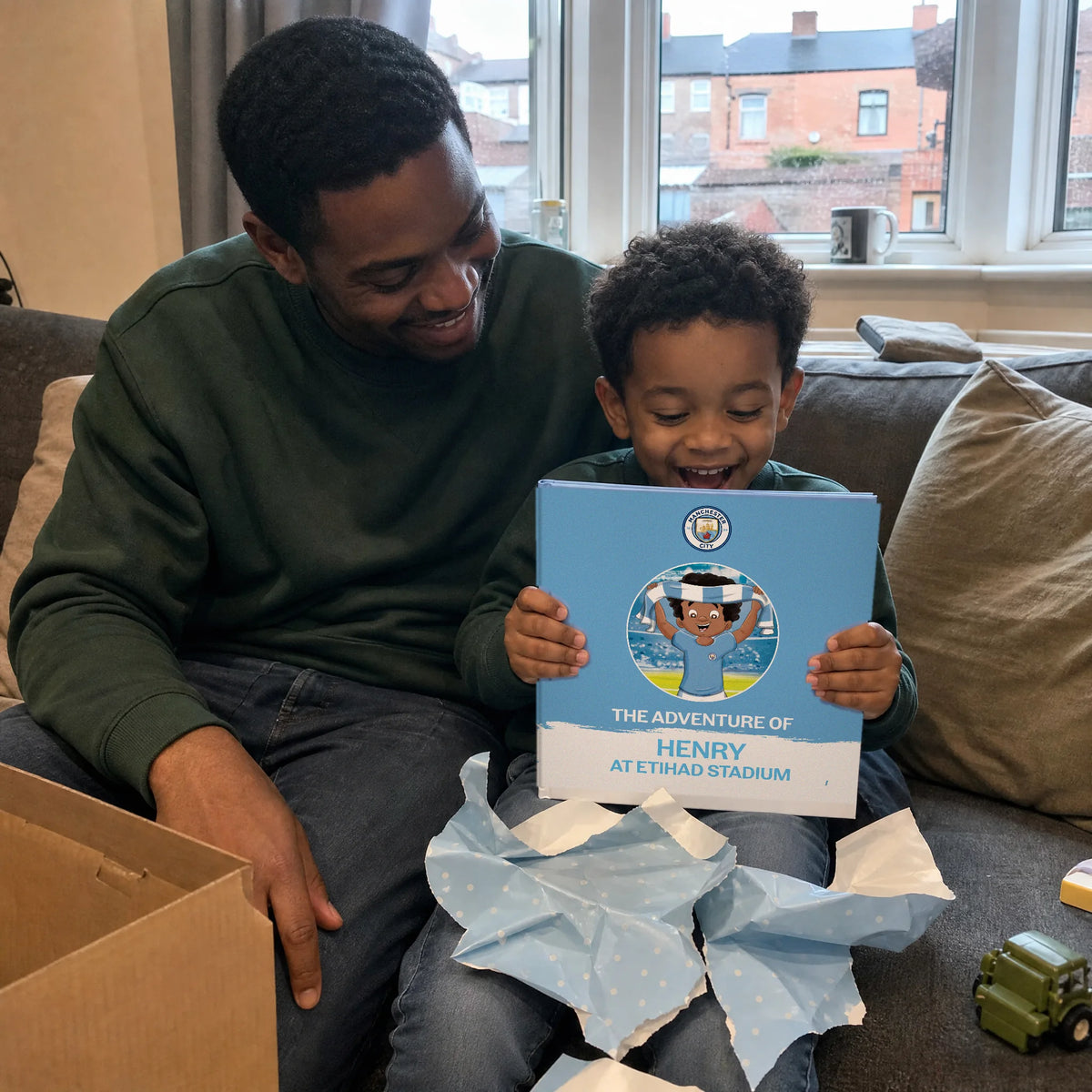 A father and son on the sofa with the Manchester City Personalised Book, just out of the wrapping paper.