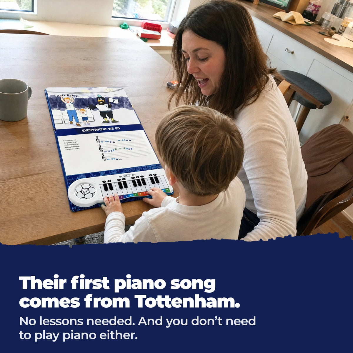 Un bambino in braccio alla mamma, al tavolo, suona i tasti del Libro di Pianoforte del Tottenham, aperto e steso davanti a loro.
