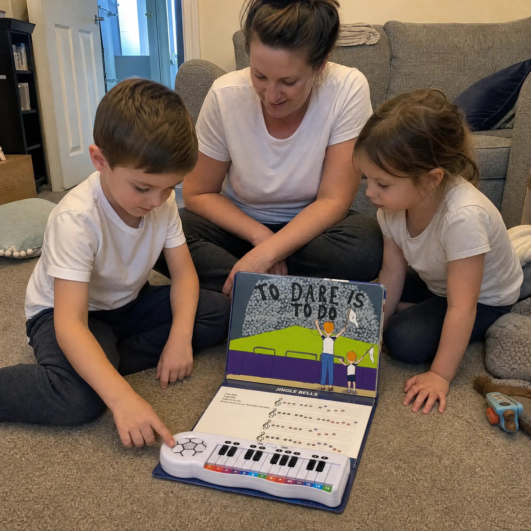 A mum and two children on the floor, the boy playing the keyboard on the open Tottenham Hotspur Piano Book.