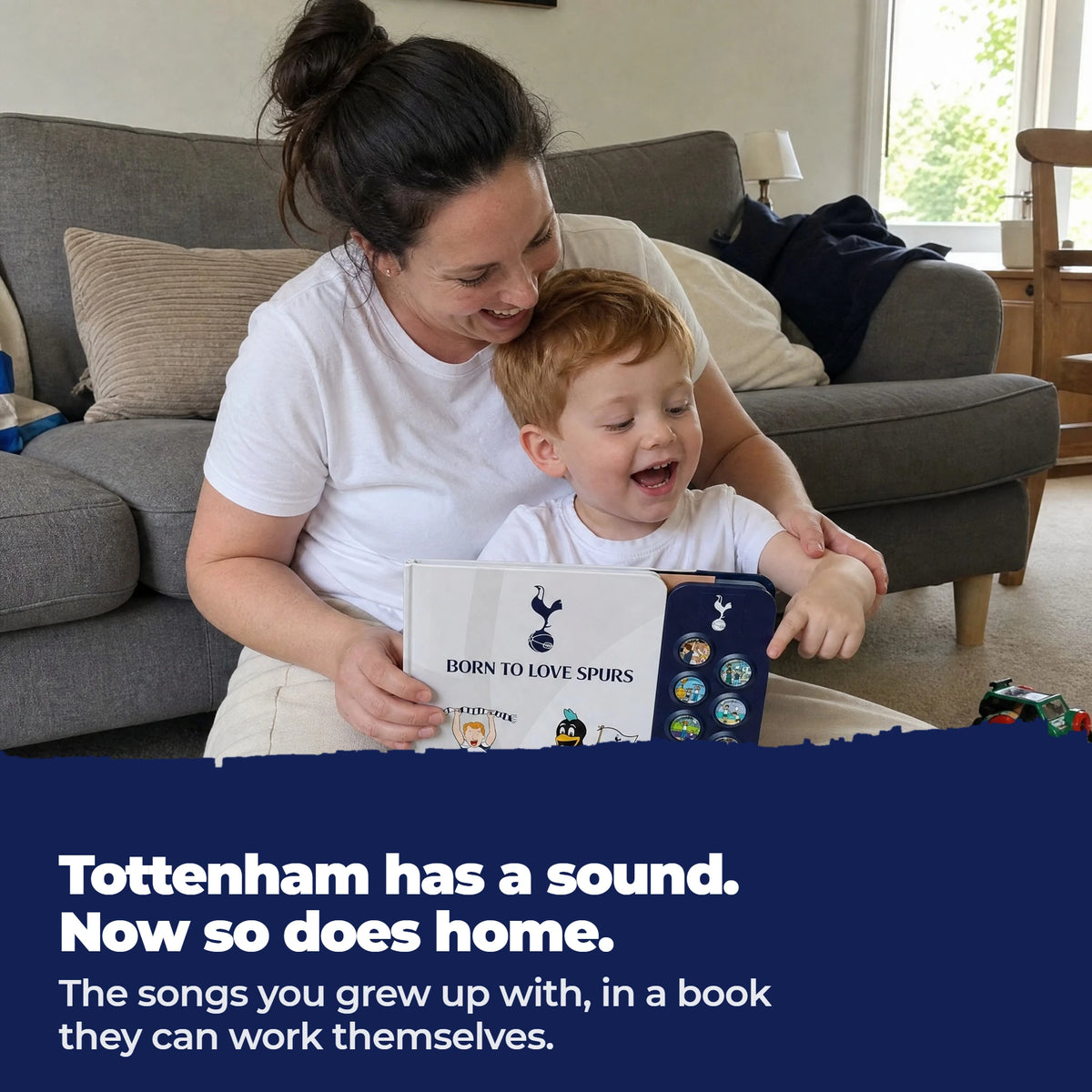 A mum and her toddler on the sofa, singing together over the open Tottenham Hotspur Sound Book, the toddler's finger on one of the sound buttons.
