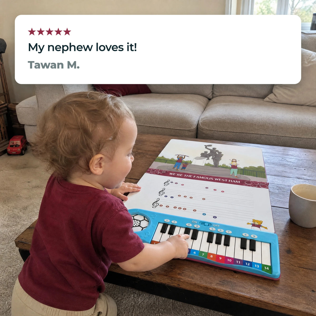 A toddler at a low table playing the keys of the West Ham United Piano Book, which lies open flat, beneath a five-star review from Tawan M.: "My nephew loves it!"