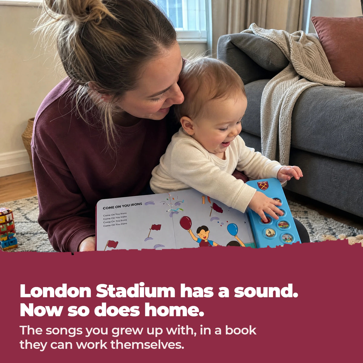 A mother and her baby on the living-room floor with the open West Ham United Sound Book, the baby's hand on the sound buttons.