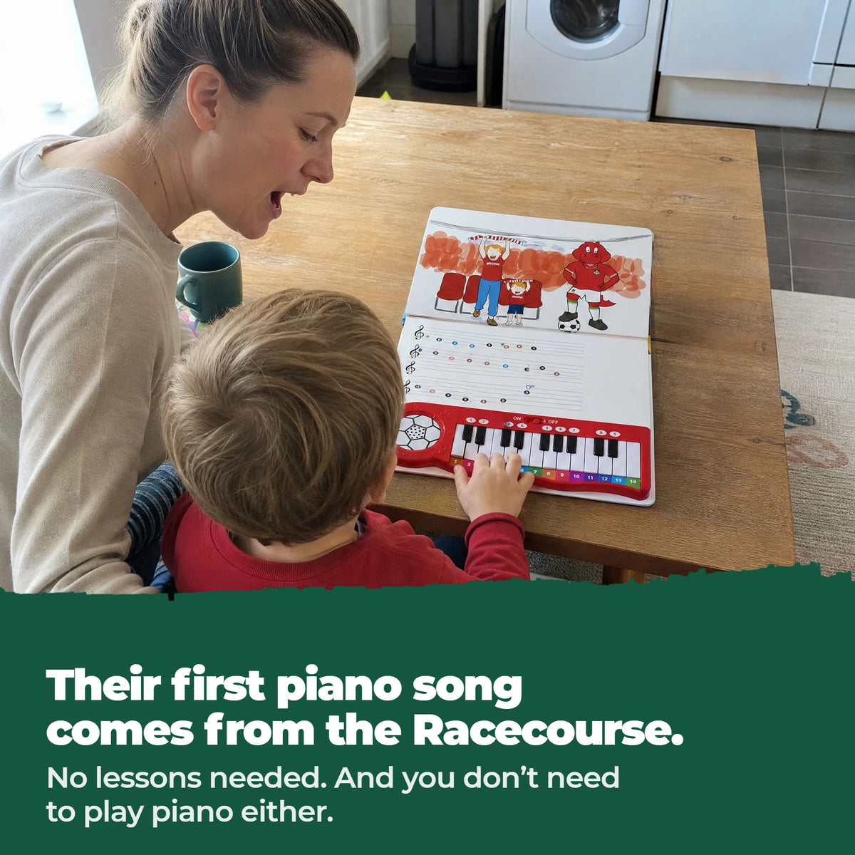 A young child on a parent's lap at a table, playing the keys of the Wrexham AFC Piano Book, which lies open flat in front of them.