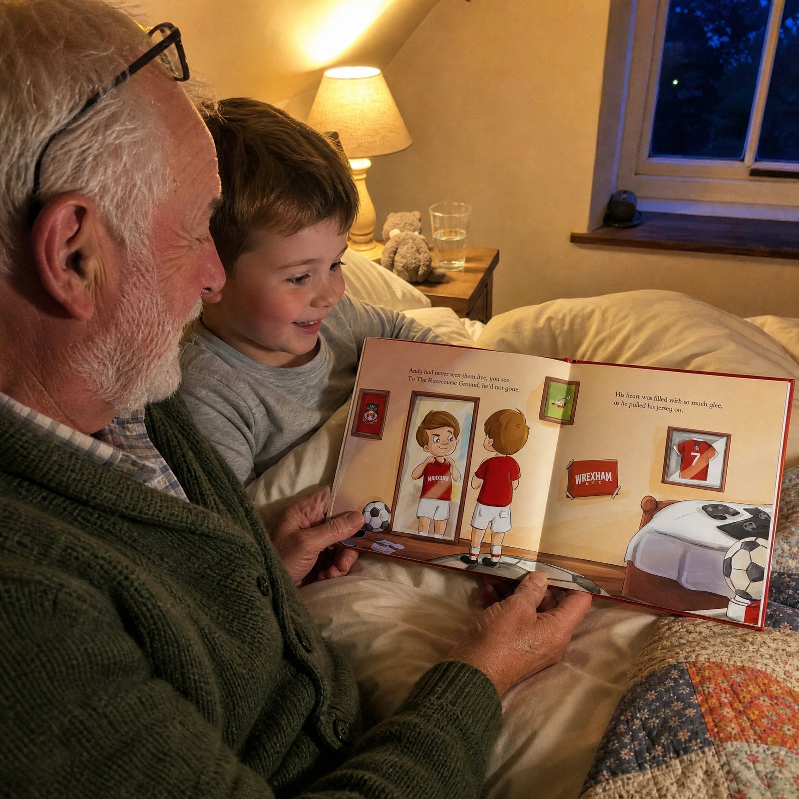 A grandad and his young grandson in bed at night reading the Wrexham AFC Personalised Book together, the boy smiling at the page.